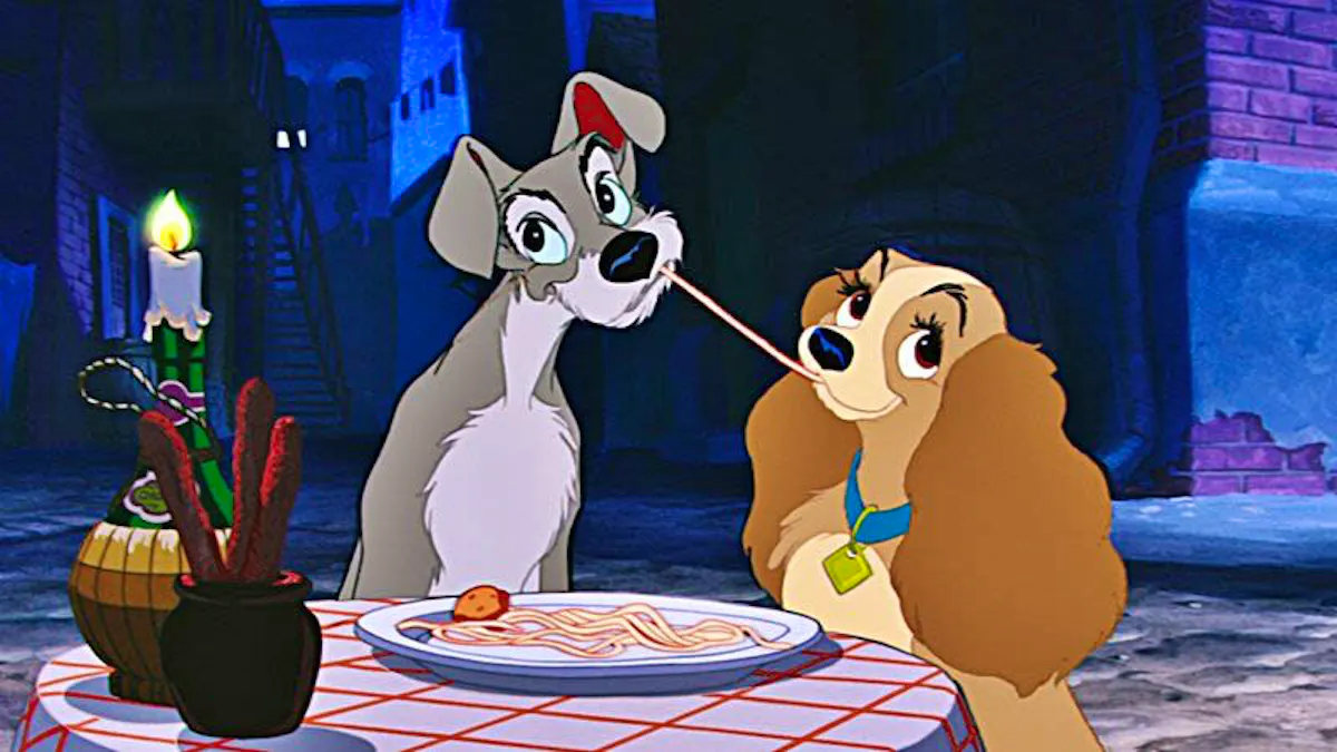 Tramp, a grey mutt, and Lady, a cocker spaniel, share a plate of spaghetti at a table in an alley