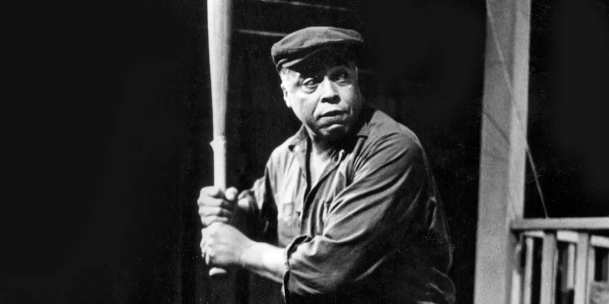 Troy, a middle aged man in a flat cap holds a baseball bat