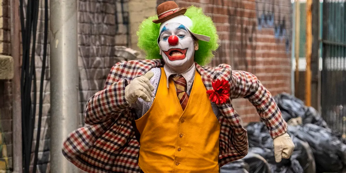Joaquin Phoenix, dressed as a clown, running through an alley in despair