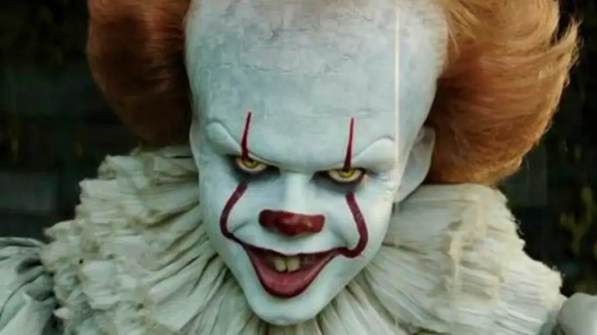 Pennywise, a demonic creature masquerading as a clown, smiles sinisterly at the screen