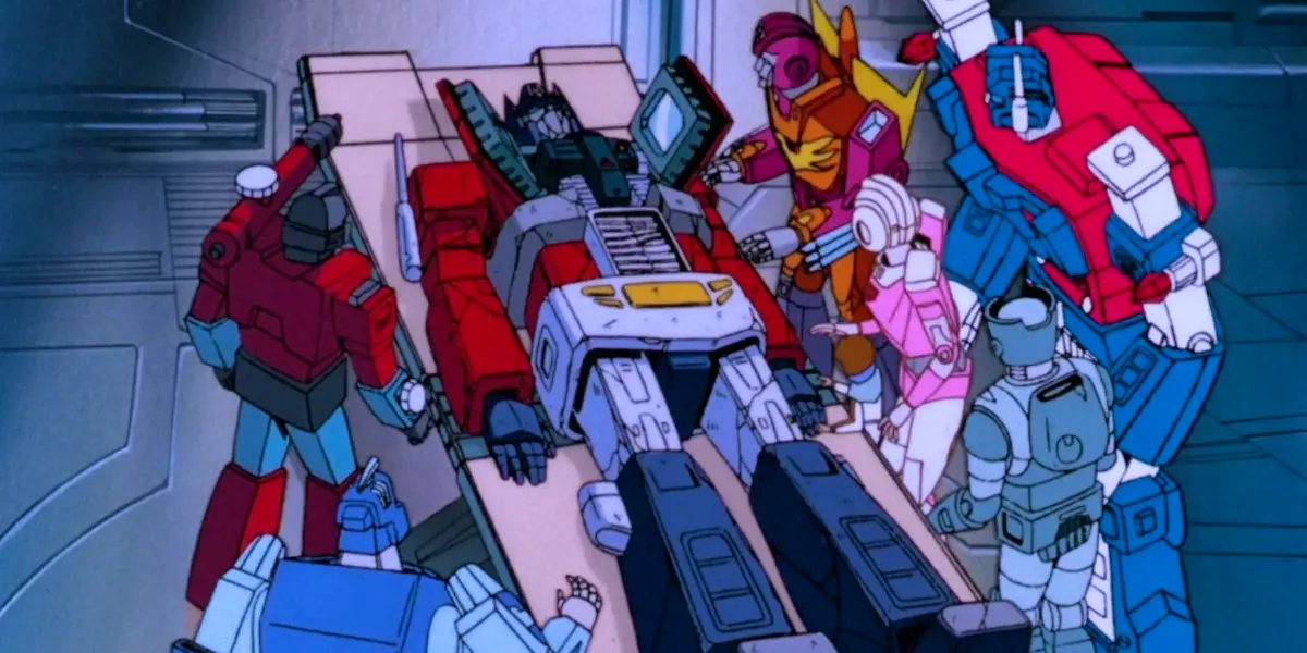 Optimus Prime, dead on a slab, surrounded by his comrades Perceptor, Blur, Hot Rod, Arcee, Spike, Kup and Ultra Magnus
